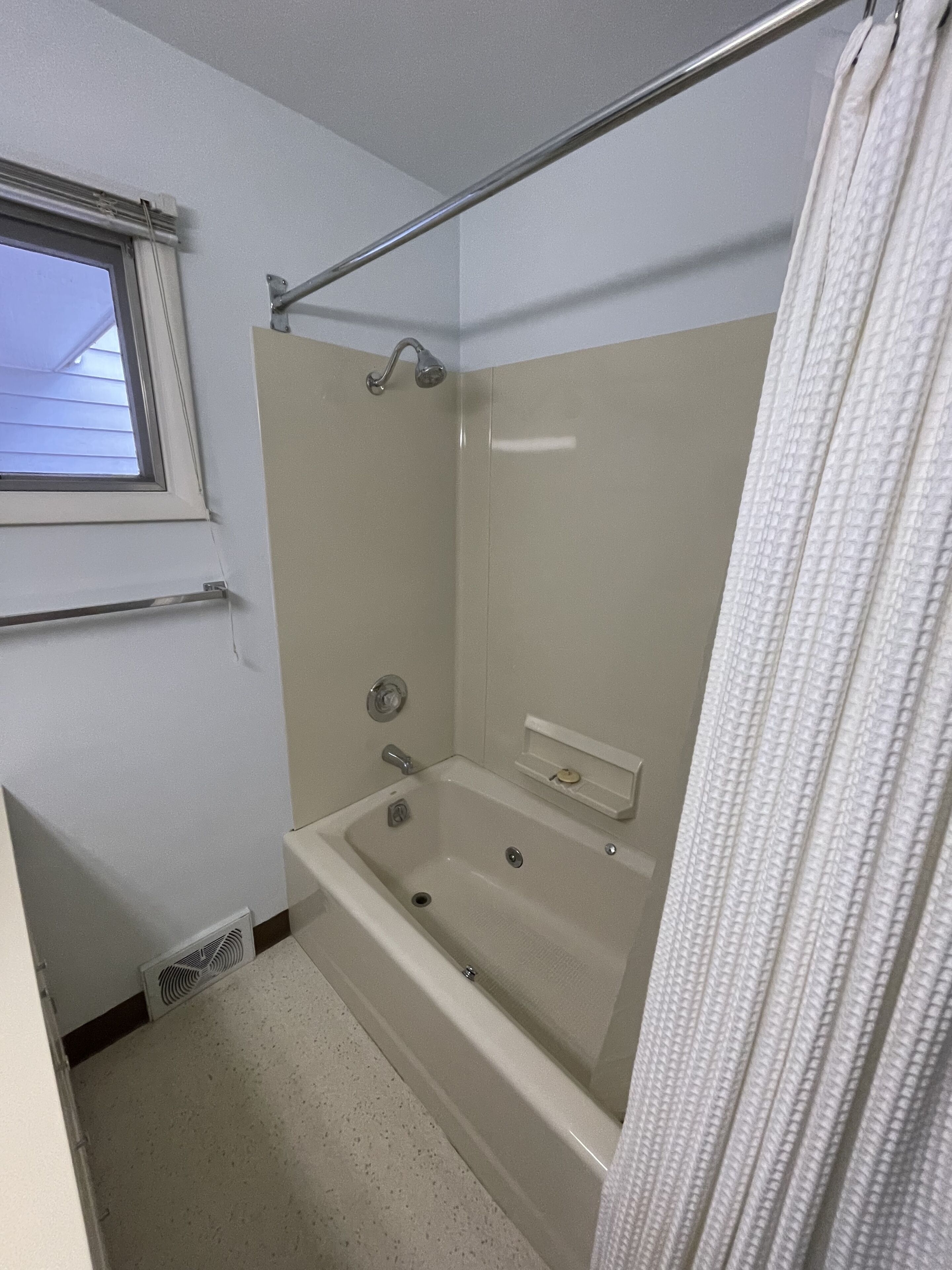 A bathroom with a bathtub, a window, a towel rack, and a shower curtain.