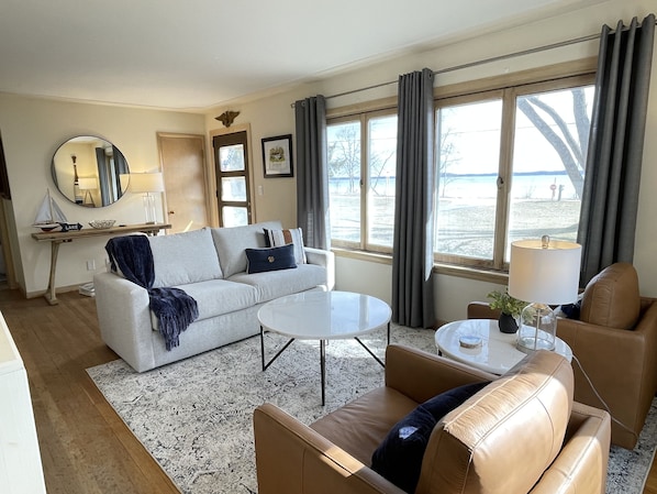 A living room with a sofa, two armchairs, a coffee table, a side table with a lamp, a mirror, and a view of the beach.