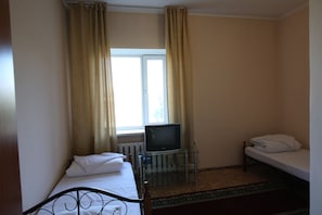 A small room with a bed, a TV on a glass stand, a window with curtains, and a radiator. - Hotel Alkuat (Astana)