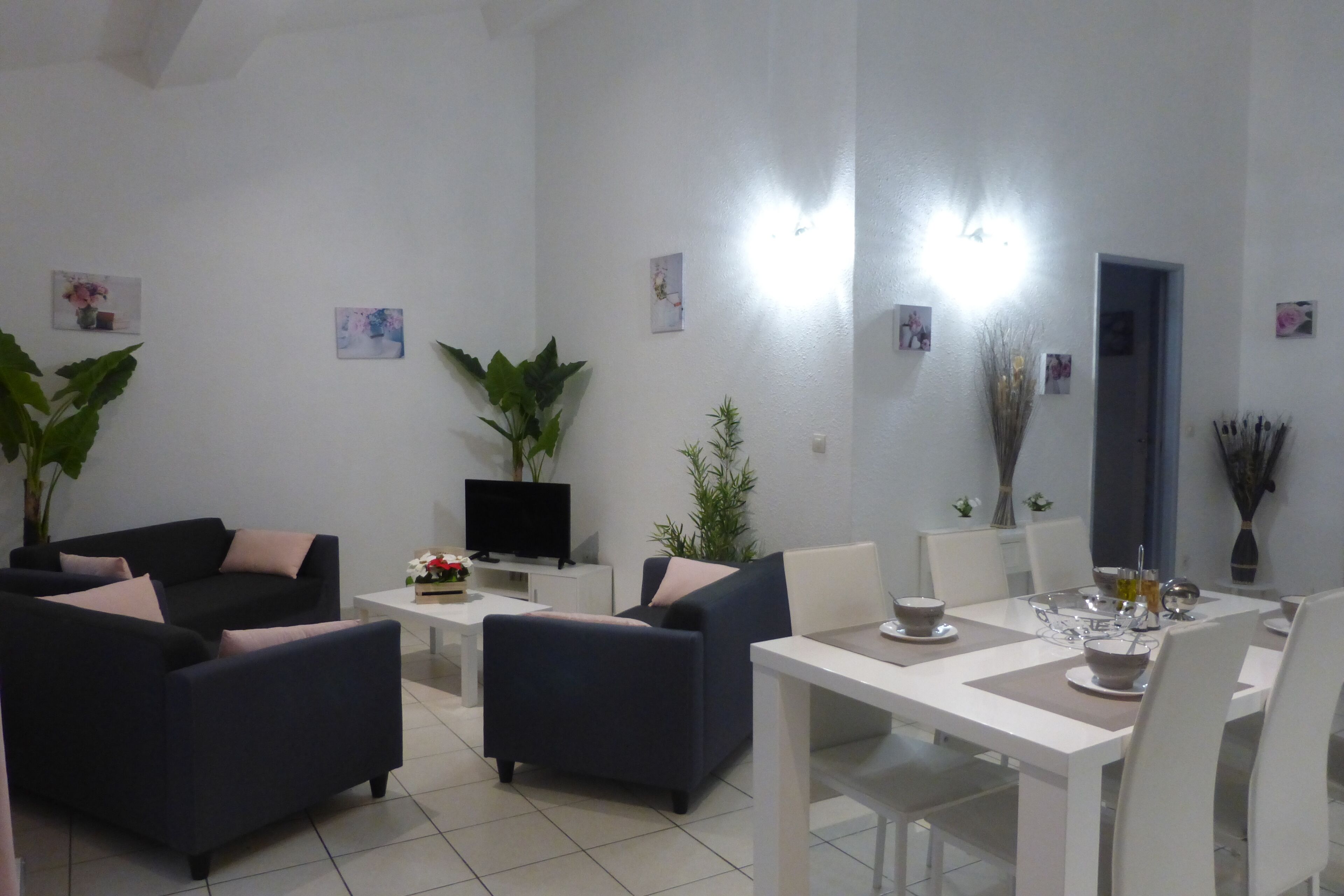 Una sala de estar moderna con comedor, que incluye sofás, un televisor y una mesa de comedor con platos y vasos.