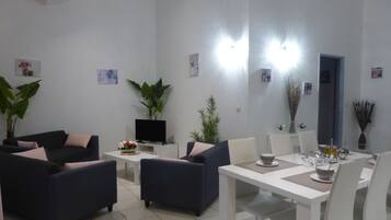 Una sala de estar moderna con comedor, que incluye sofás, un televisor y una mesa de comedor con platos y vasos.
