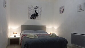 A bedroom with a bed, two bedside tables with lamps, a radiator, and wall art.