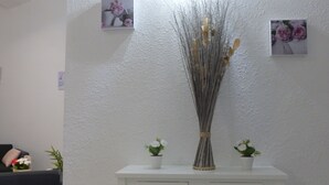 A white wall with two small potted plants and a tall vase of branches.