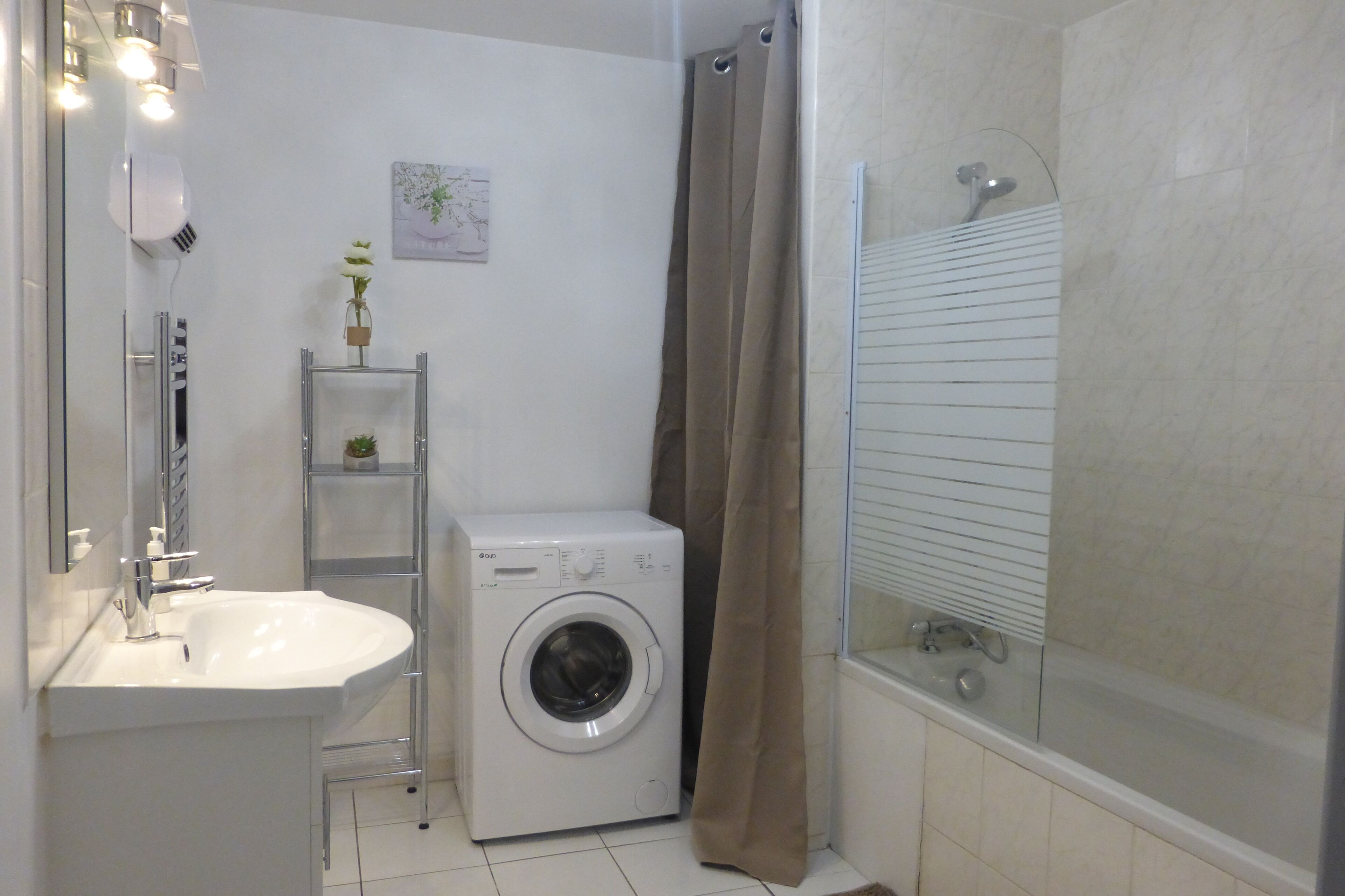 A compact bathroom with a washing machine, a sink, and a shower area.