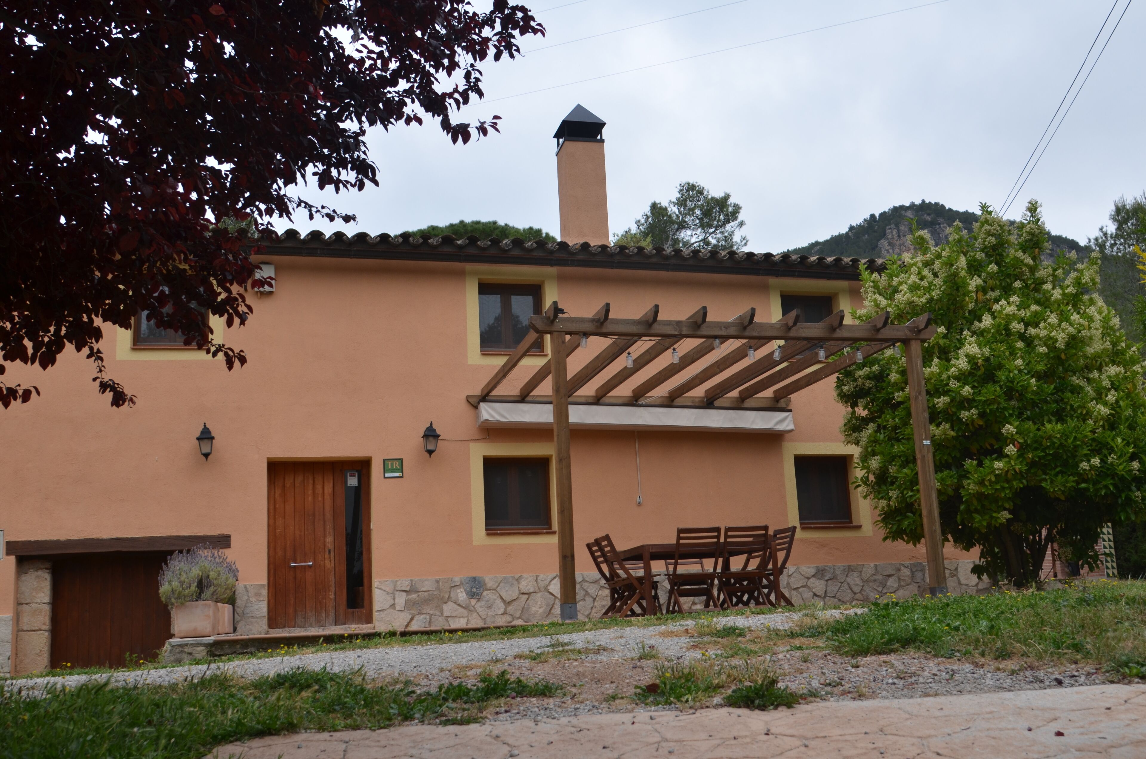Un bâtiment à deux étages doté d’une pergola en bois, de fondations en pierre et d’une cheminée.