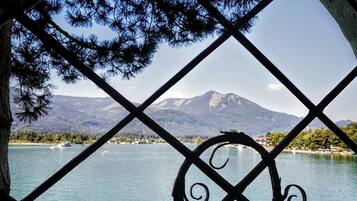 A view through a metal fence with a decorative pattern, overlooking a lake with mountains in the background.