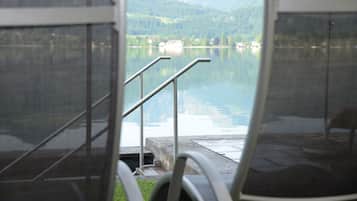 A view from a window with metal railings overlooking a calm lake and mountains.
