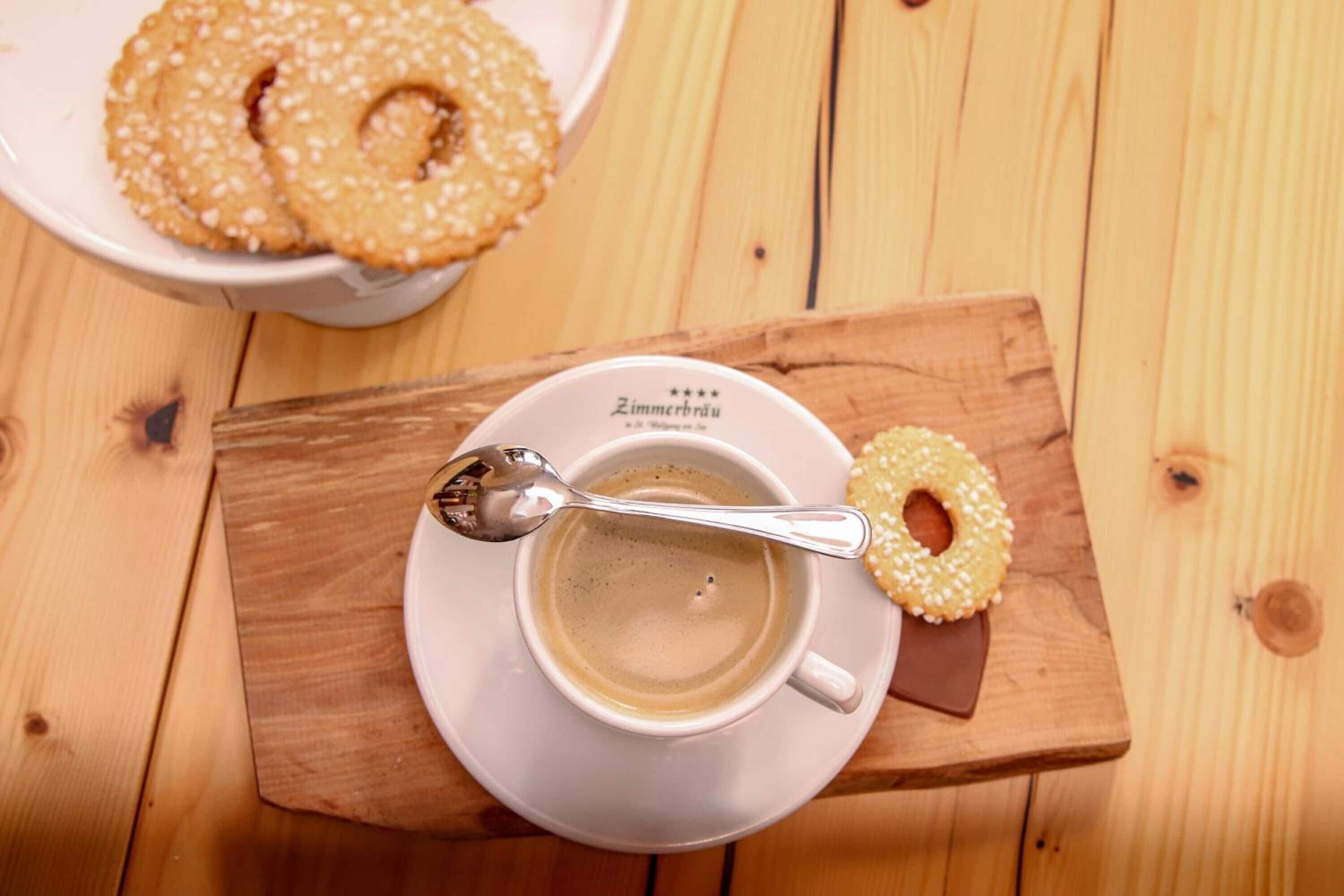 Una taza de café sobre una bandeja de madera, con una cuchara y una rosquilla.