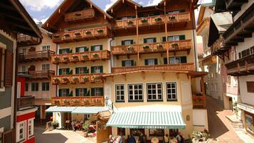 A traditional European hotel with multiple balconies, outdoor seating, and a sign indicating it is a restaurant.