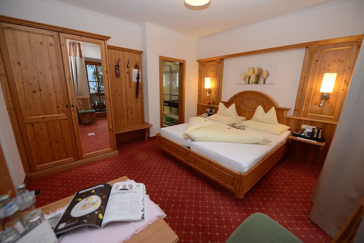 Une chambre d’hôtel avec un lit en bois, un bureau avec un magazine, un miroir et des armoires en bois.
