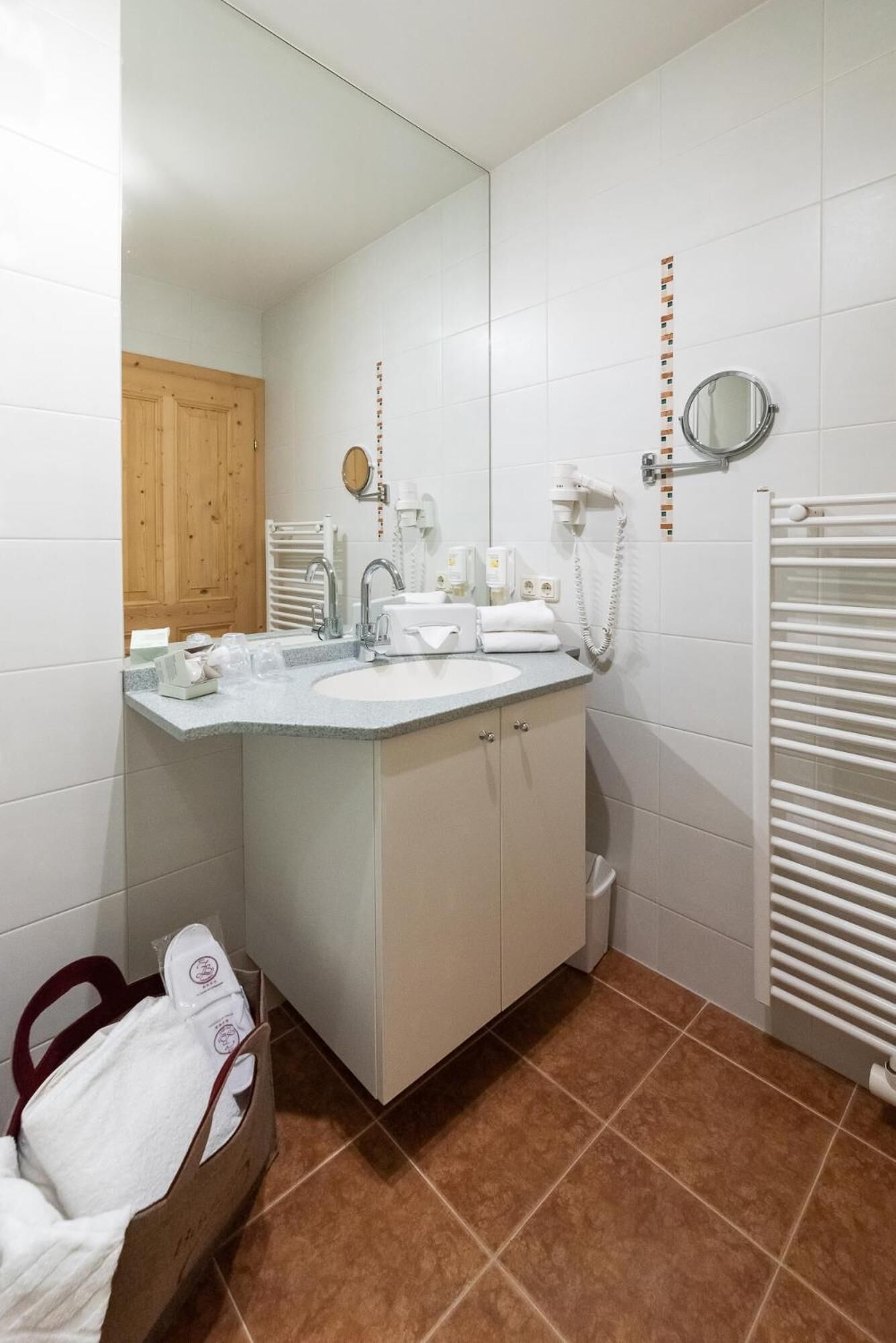 Een badkamer met een wastafel, spiegel, handdoekrek en een houten deur.