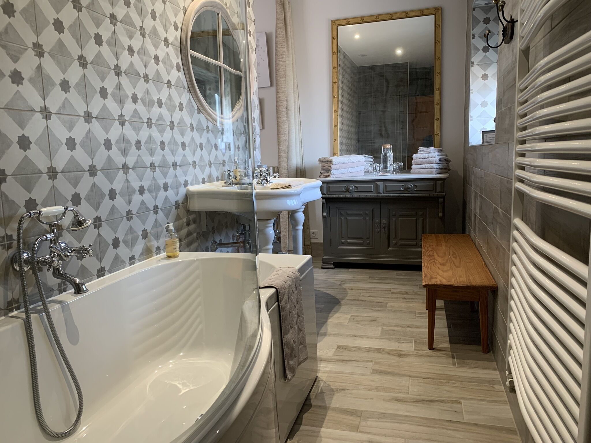 A bathroom with a freestanding bathtub, a sink, a mirror, and a bench.