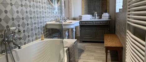 A bathroom with a freestanding bathtub, a sink, a mirror, and a bench.