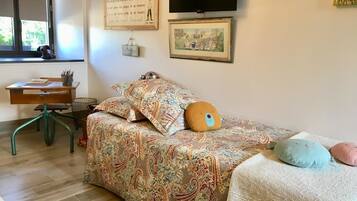A bedroom with a patterned bedspread, a desk with books and a lamp, and a window with a view.