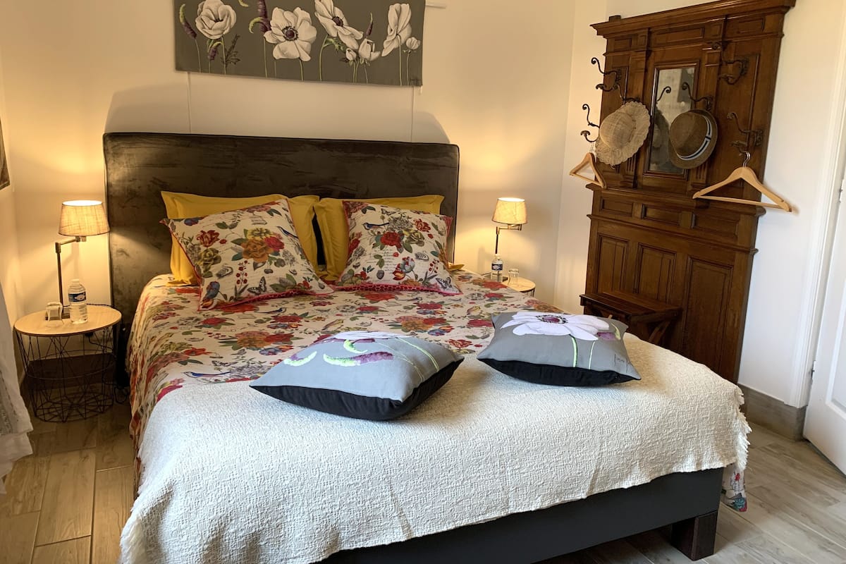 A bed with floral bedding, two pillows, a wooden headboard, and a wall-mounted mirror.