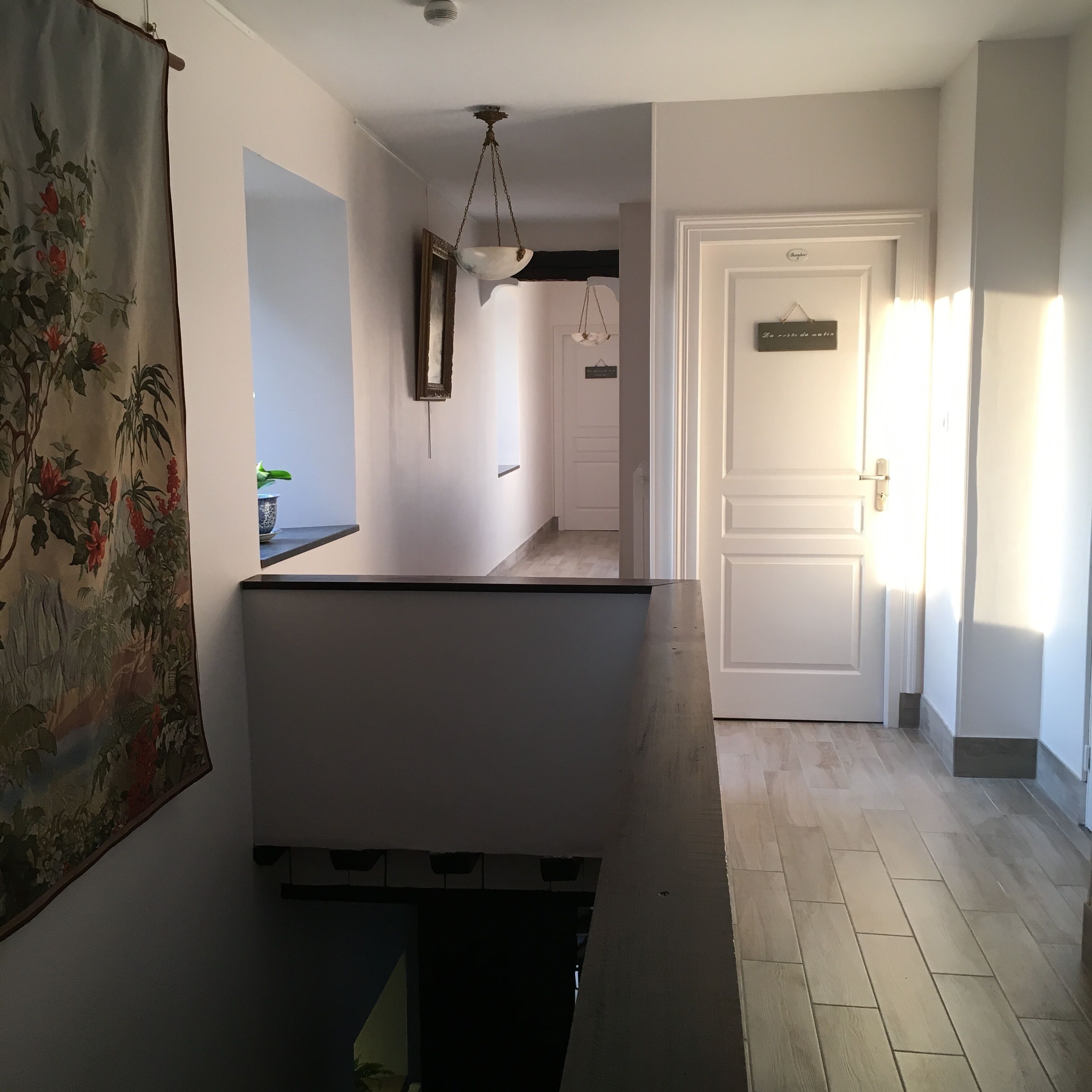 Un pasillo con una puerta blanca, una lámpara colgante y un espejo instalado en la pared.