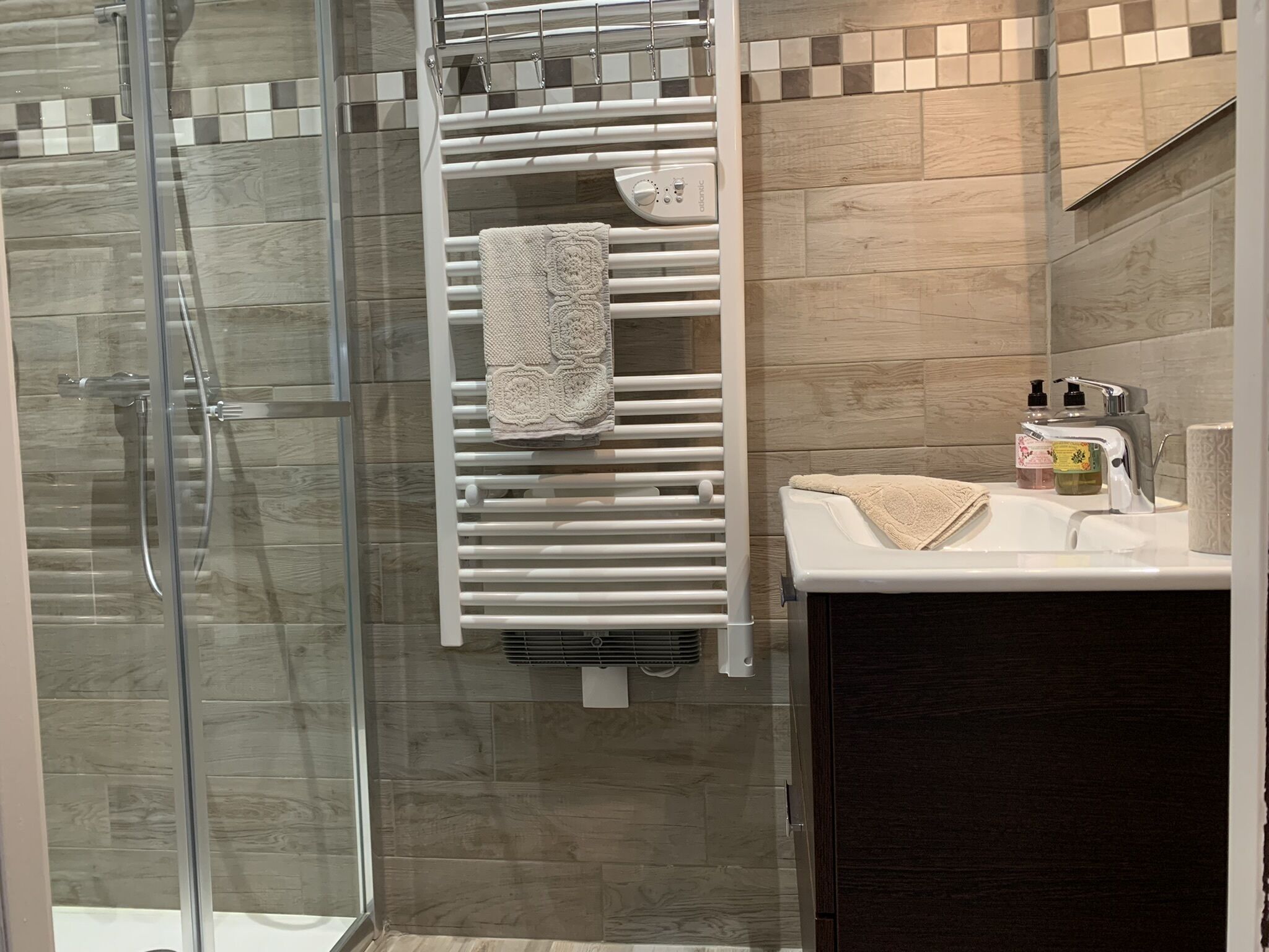 Une salle de bain moderne avec une douche à parois de verre, un porte-serviettes blanc et un lavabo avec des articles de toilette.