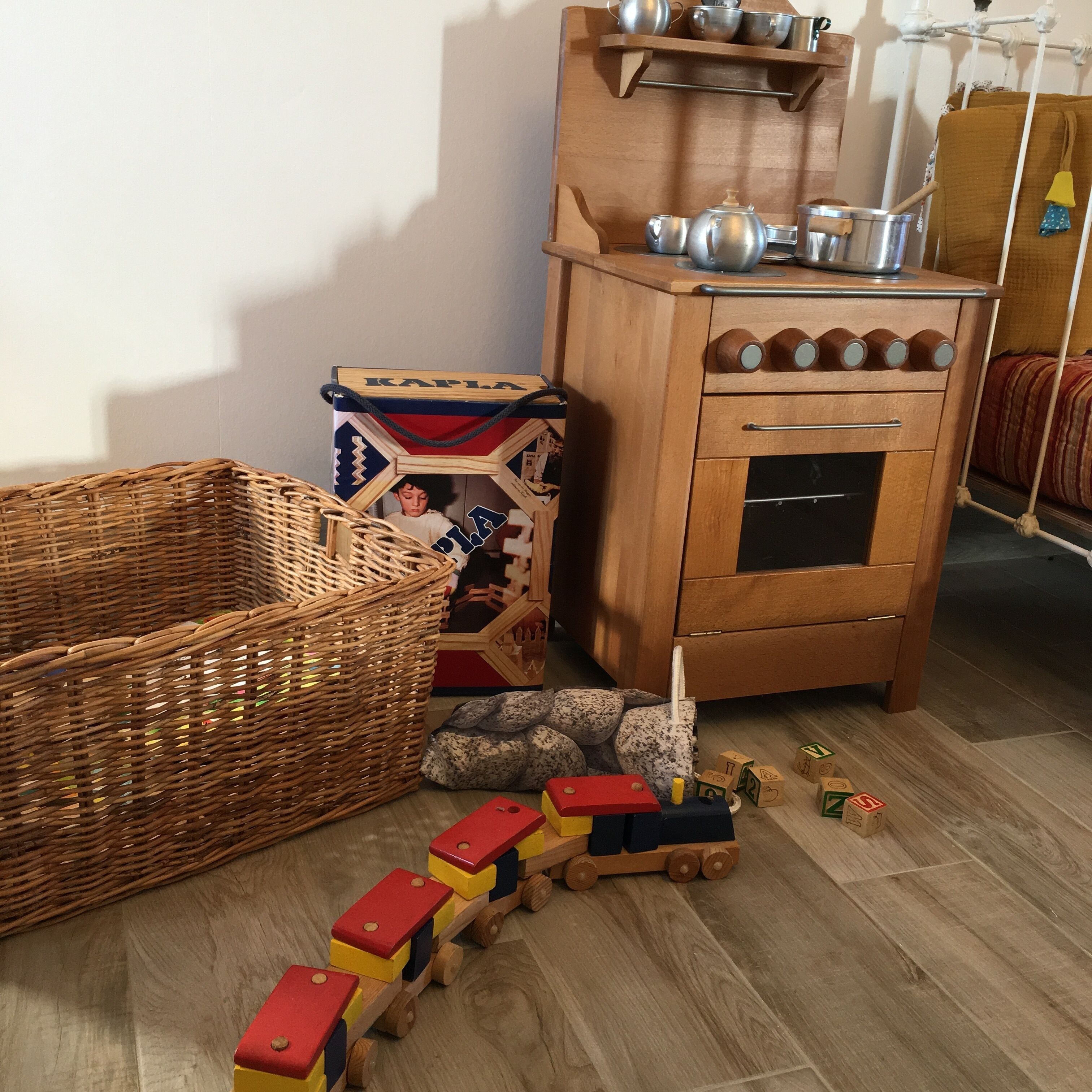 A wooden cabinet with kitchenware, a wicker basket, and a toy train on a wooden floor.