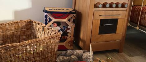 A wooden cabinet with kitchenware, a wicker basket, and a toy train on a wooden floor.
