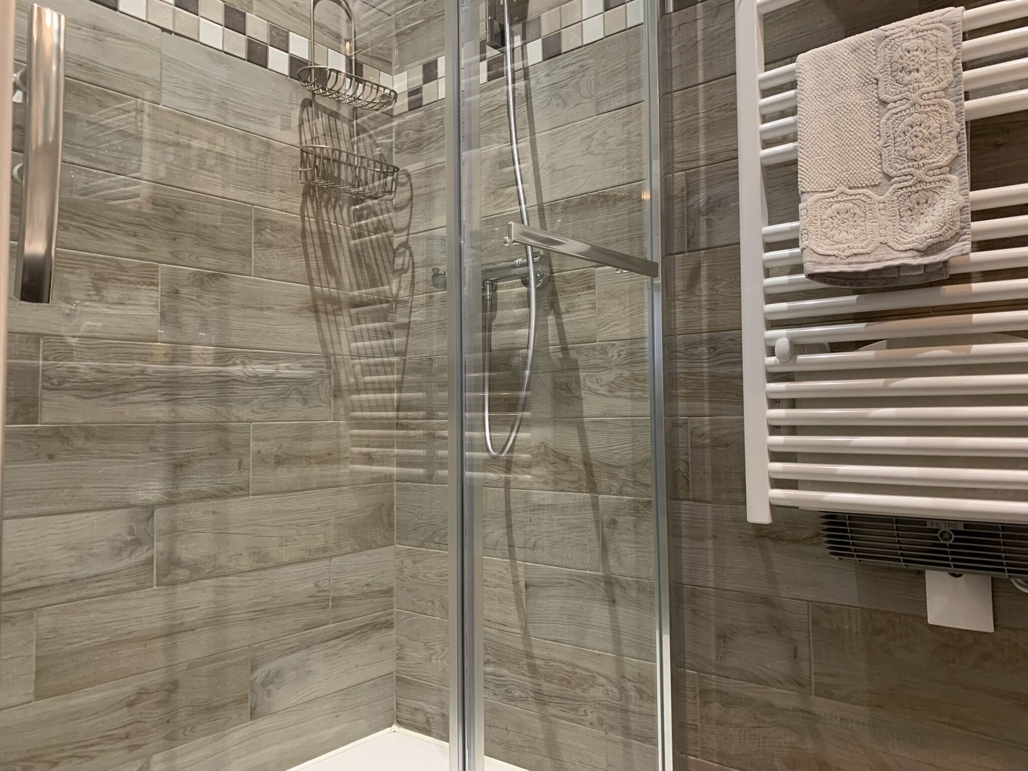 A shower with a glass door, a towel rack, and a wall with a checkered pattern.