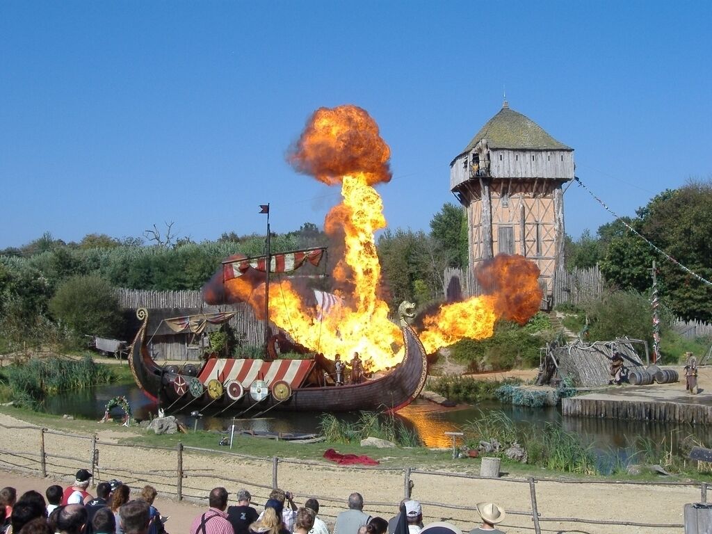 A Viking ship on fire with spectators in the foreground.