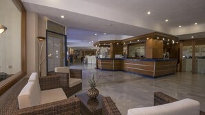 A spacious lobby with wicker furniture, a reception desk, and a glass door leading to another area. - Santa Maria Aparthotel (Adeje)
