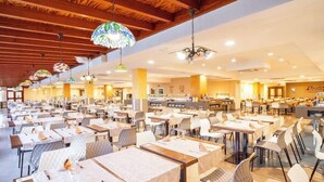 A spacious dining area with multiple tables and chairs, wooden ceiling beams, and hanging stained glass lamps. - Santa Maria Aparthotel (Adeje)