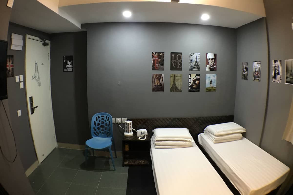 A hotel room with two beds, a desk, a chair, and a wall decorated with various posters.