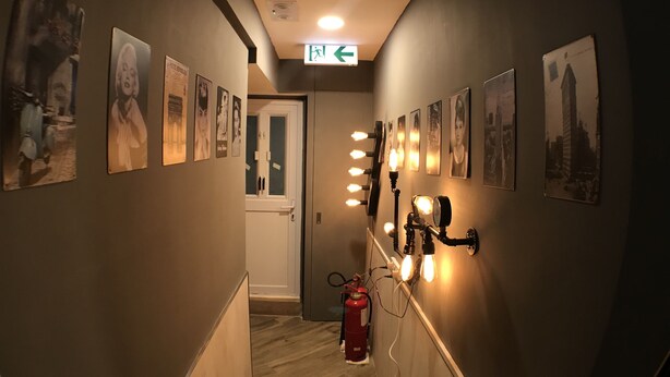 A hallway with framed pictures on the walls, a fire extinguisher, and a light fixture with multiple bulbs. - Soso Hostel (Hong Kong)