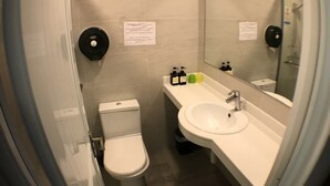 A small, modern bathroom with a toilet, sink, and mirror. There are toiletries on the sink counter. - Soso Hostel (Hong Kong)
