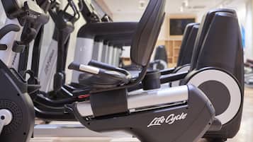 A row of stationary bikes in a gym with a wooden floor and a television in the background.