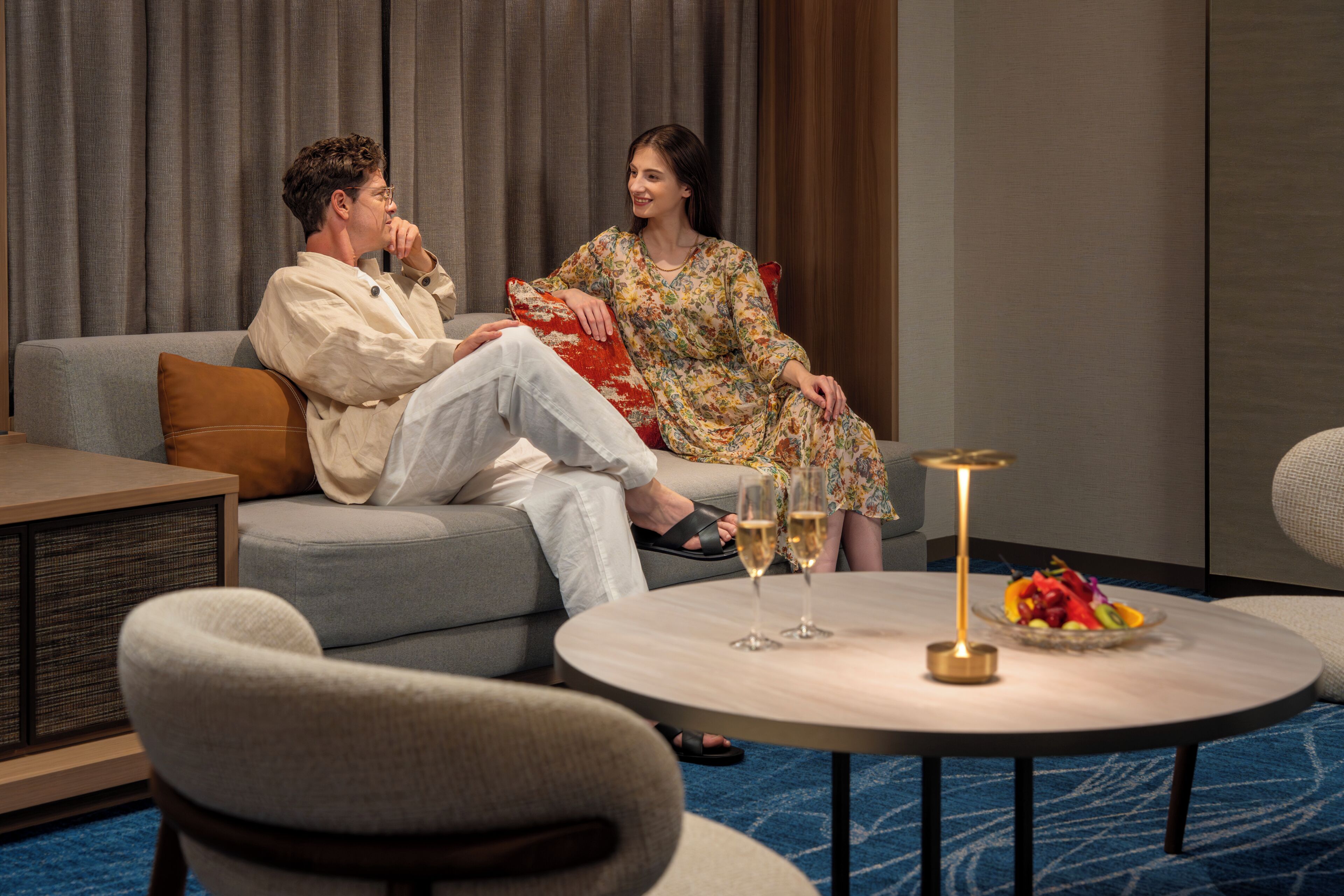A room with a sofa, a round table with drinks, and a fruit bowl.
