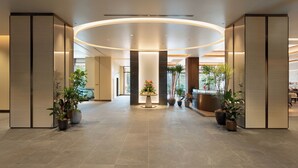 Un hall d’entrée spacieux et moderne, doté d’un plafond incurvé, de grandes plantes en pot et d’un comptoir d’accueil.