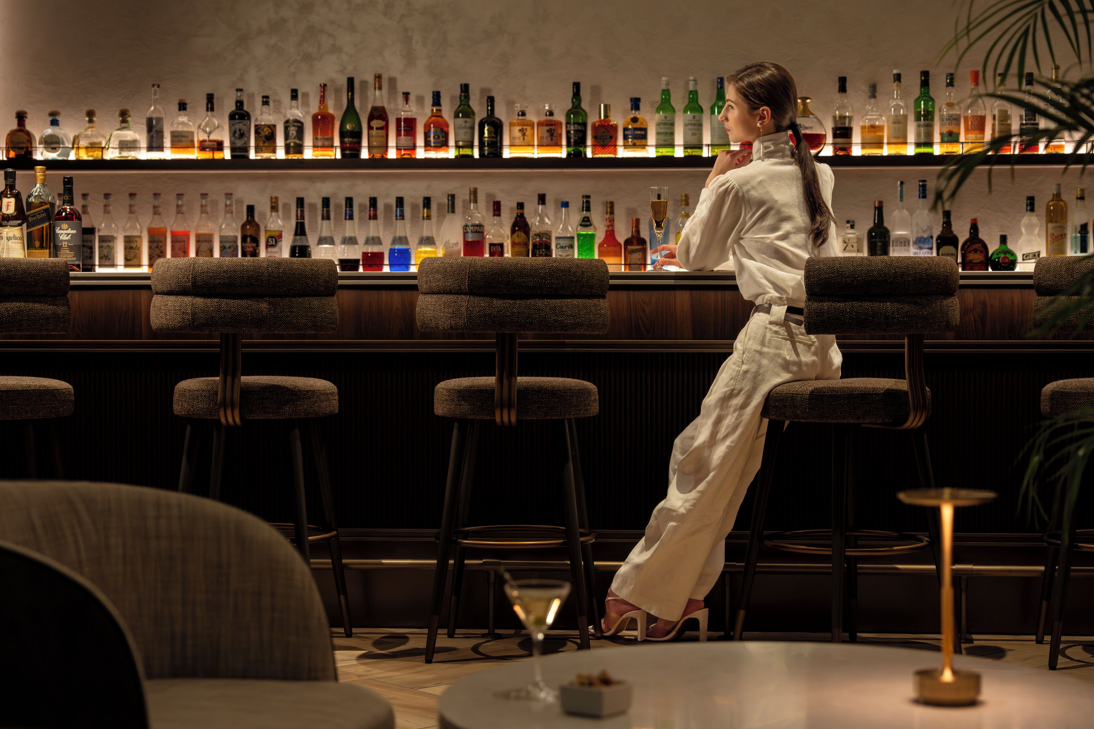 Zona de bar con taburetes, una barra y una variedad de botellas.