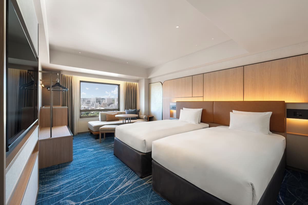 Ett hotellrum med två sängar, en sittgrupp med utsikt och ett stort fönster.