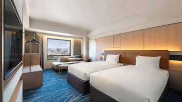 A hotel room with two beds, a seating area with a view, and a large window.