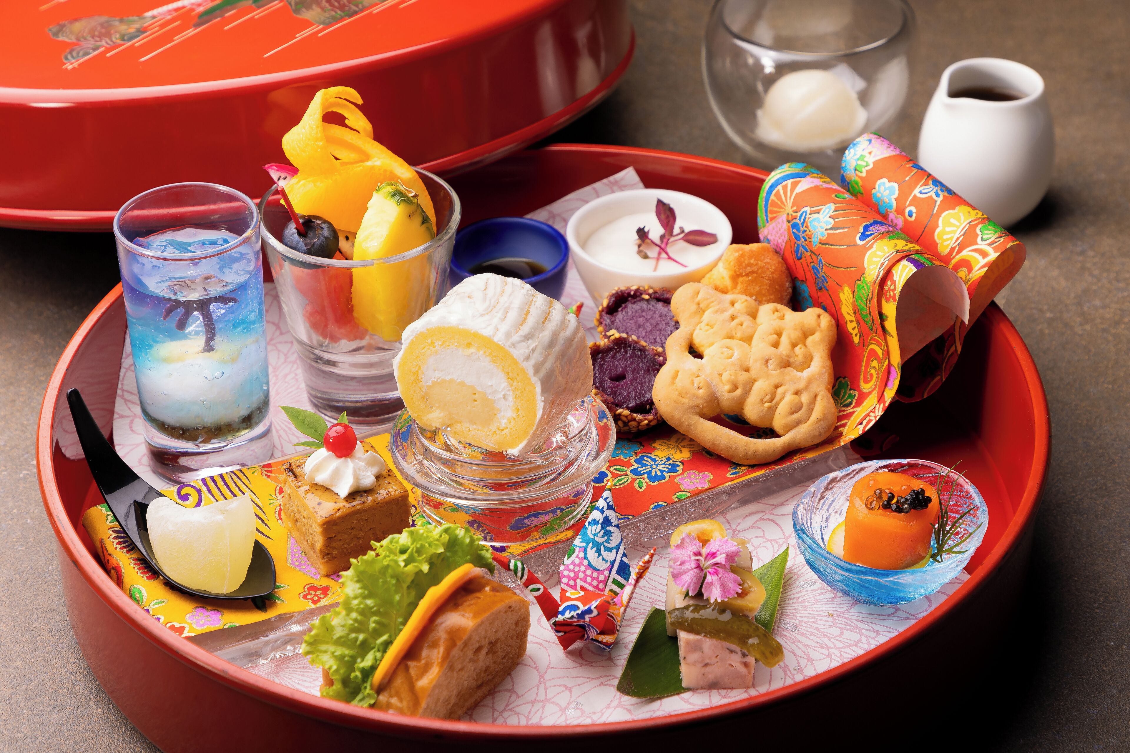 A tray with various food items including a glass of iced drink, a dessert with a cherry, and several types of pastries.
