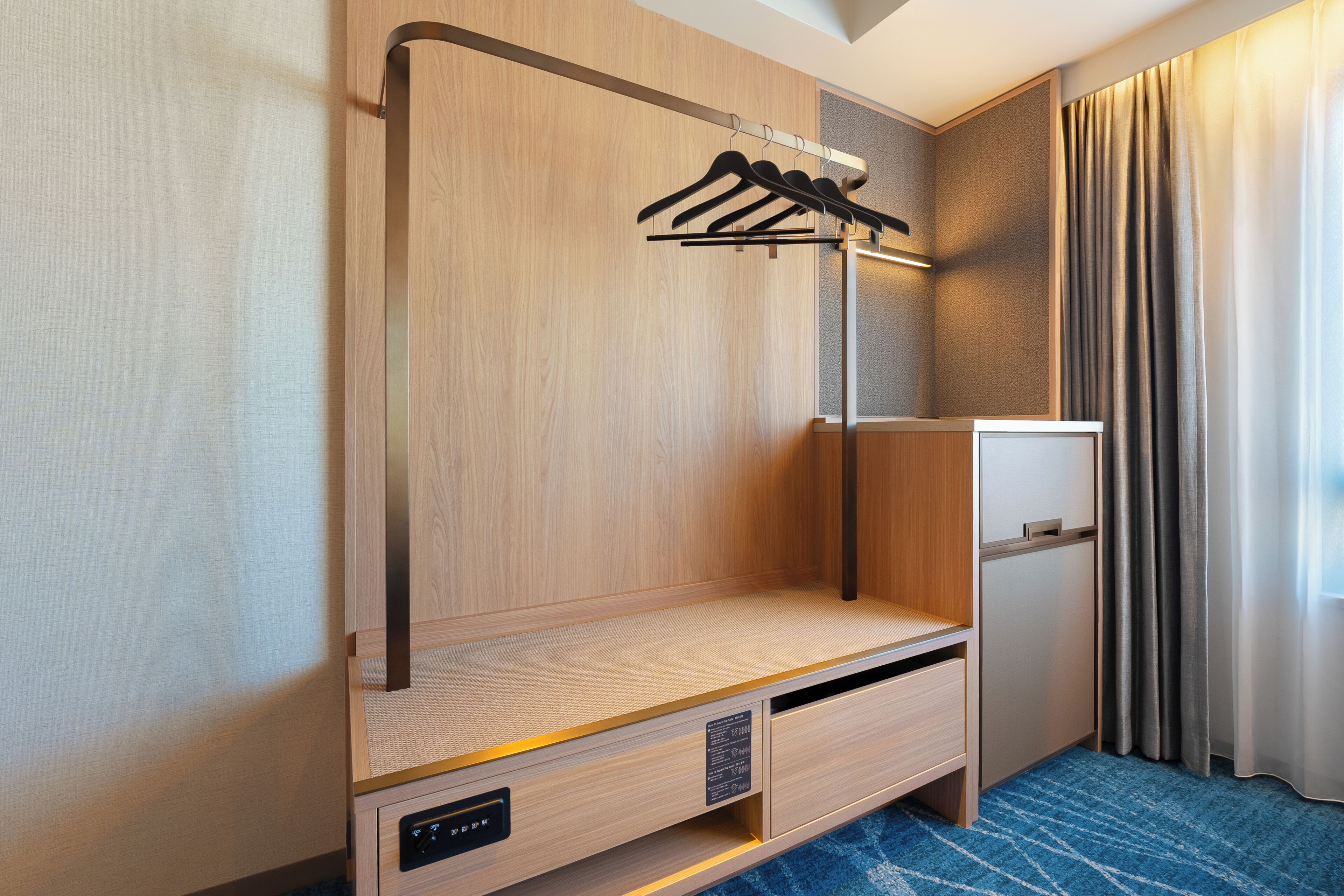 Une chambre d’hôtel compacte, dotée d’une armoire en bois, d’un petit bureau et d’un mini-réfrigérateur encastré.