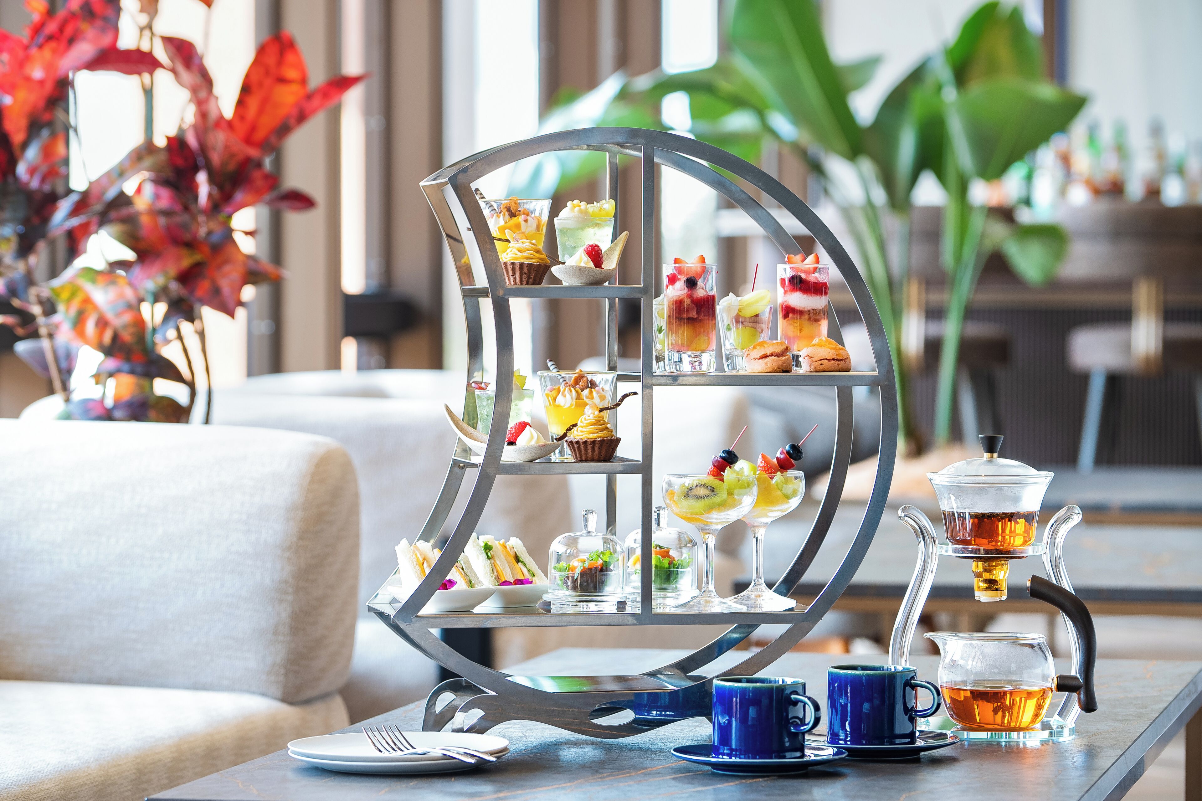 A tea service set with a tiered display stand, a blue cup, and a teapot on a table.
