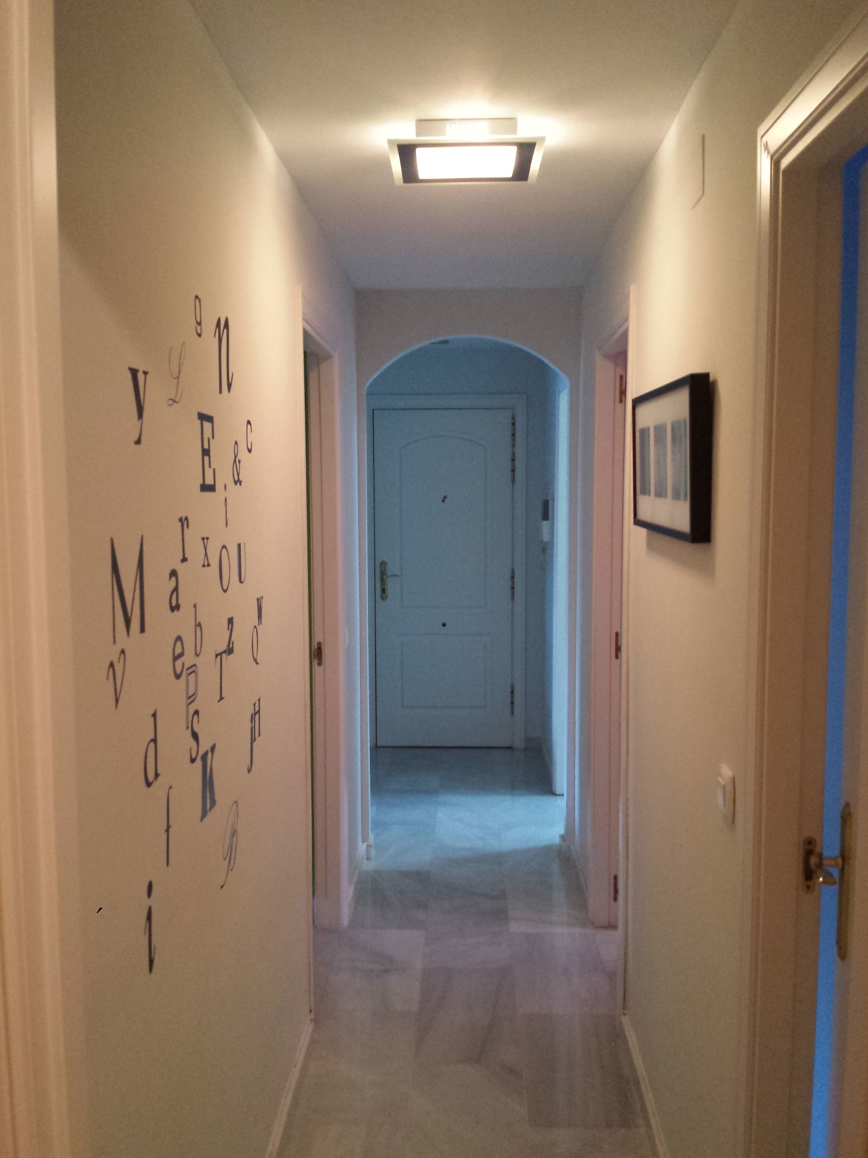A hallway with a white door at the end, a ceiling light, and a wall with letters.