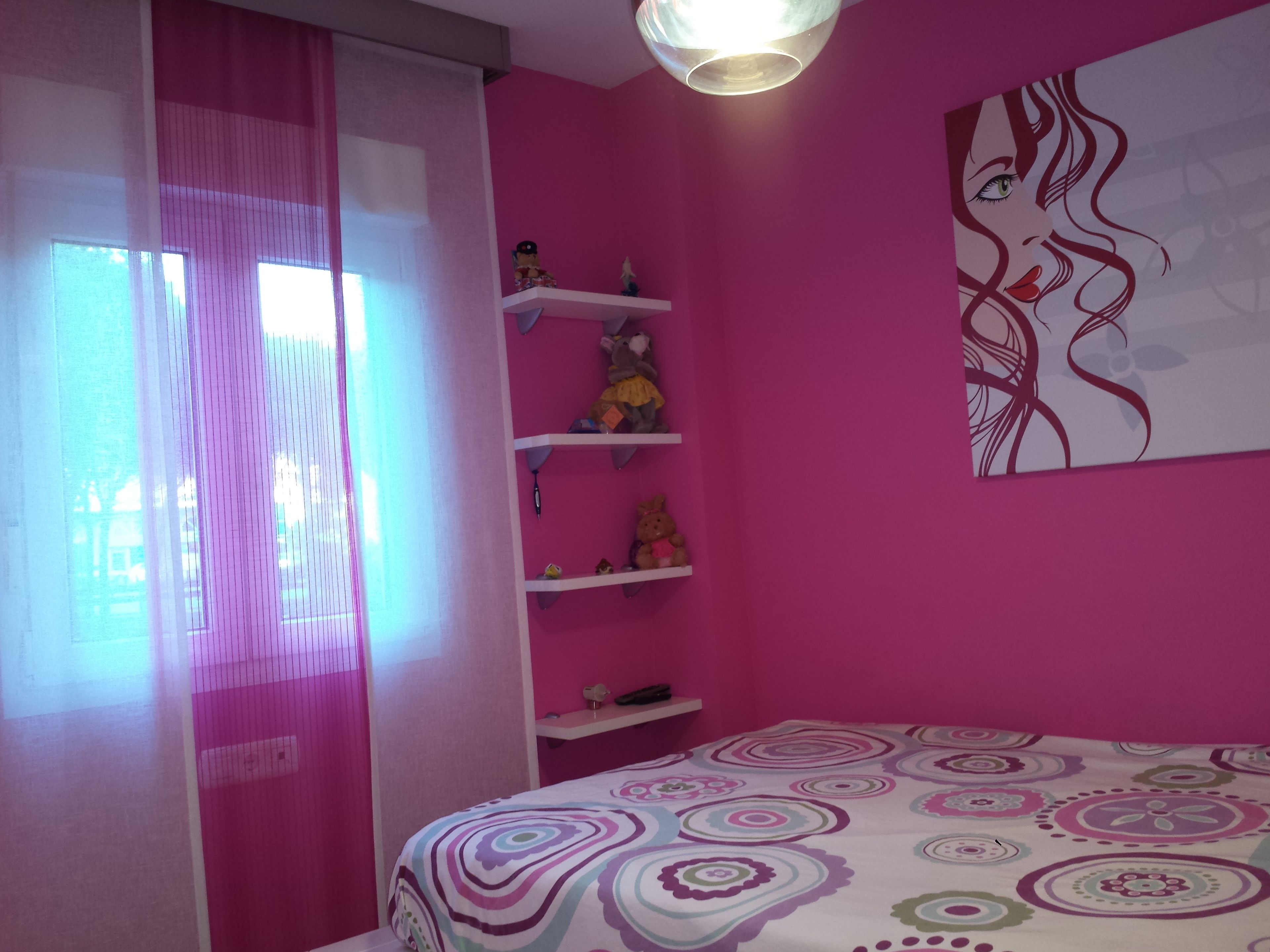 A pink-themed bedroom with a bed, shelves with toys, and a wall art piece.