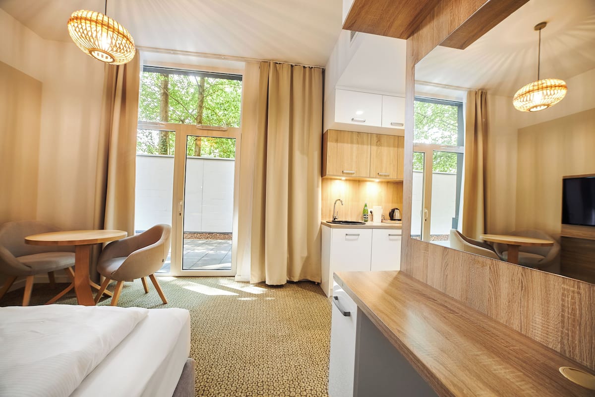 Ein Hotelzimmer mit Bett, Esstisch, Stuhl, Küchenzeile und großen Fenstern.