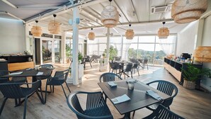 Un espace de salle à manger moderne, avec des chaises et des tables noires, de grandes fenêtres et des luminaires en matériaux tressés.