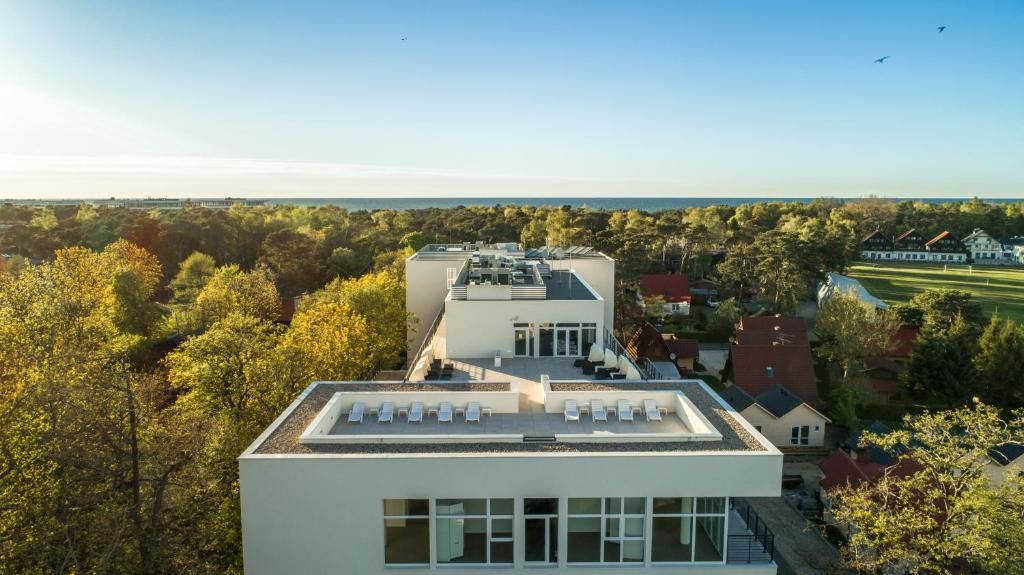 Ein modernes Gebäude mit flachem Dach, großen Fenstern und einer Dachterrasse mit Liegestühlen.