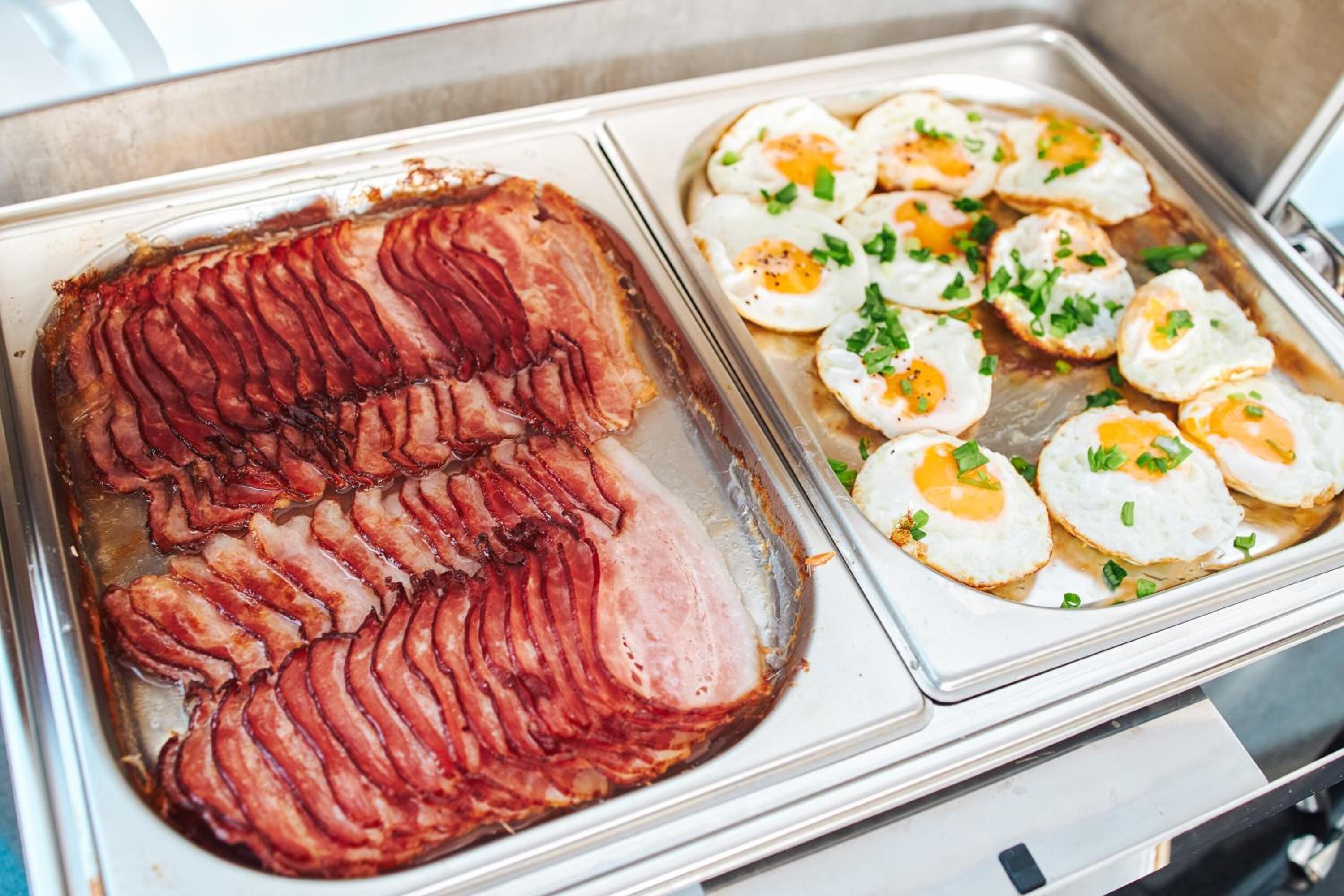 Un bufé con jamón en rodajas y huevos fritos, adornado con hierbas aromáticas.