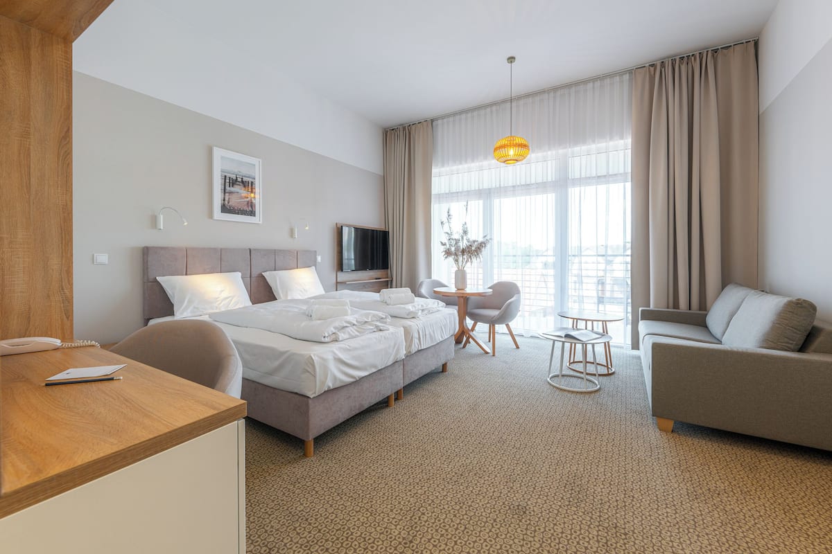 Ein Hotelzimmer mit Bett, Schreibtisch, Sofa, Fernseher und einem Fenster mit Vorhängen.