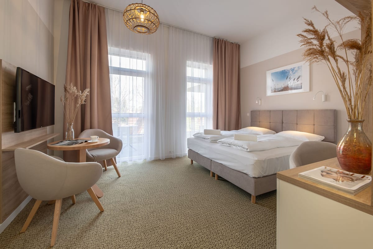 Ein Hotelzimmer mit Bett, Schreibtisch, Stuhl, Fernseher und einem großen Fenster mit Vorhängen.