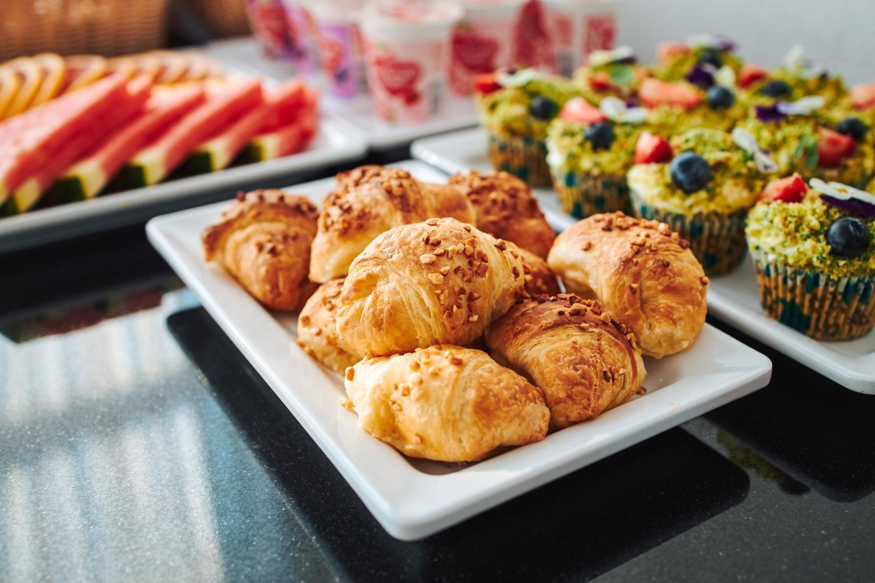 Un bufé con diversas opciones de pastelería y postres, incluyendo croissants y cupcakes.