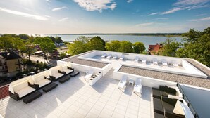 Une terrasse sur le toit, dotée de chaises longues et d’un espace piscine, offrant une vue sur une étendue d’eau et la végétation environnante.