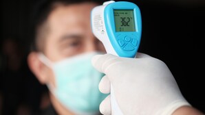 A person holding a digital thermometer with a display reading 32°C.